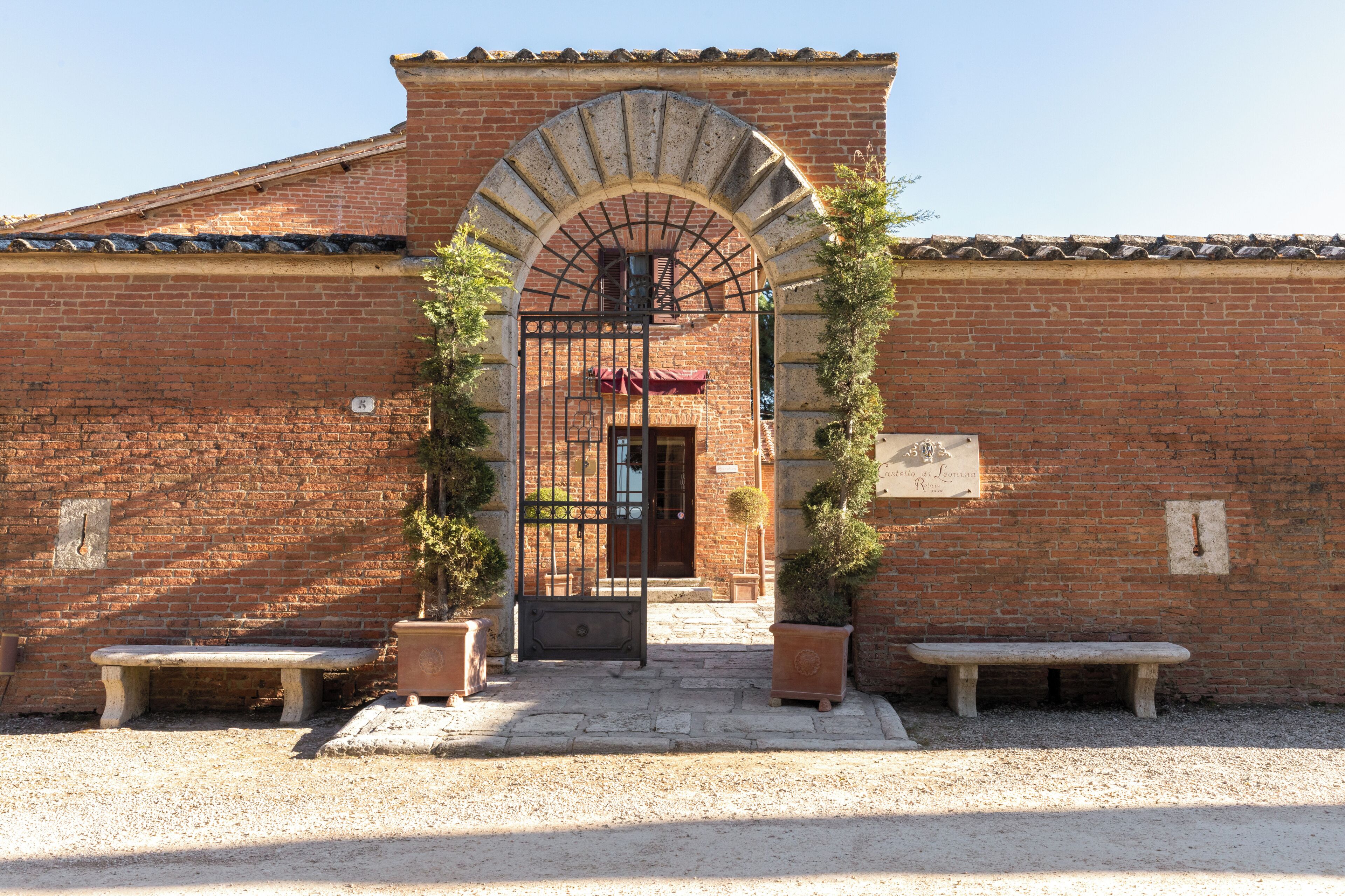 A brick building with a large arched entrance, two benches, and potted plants.