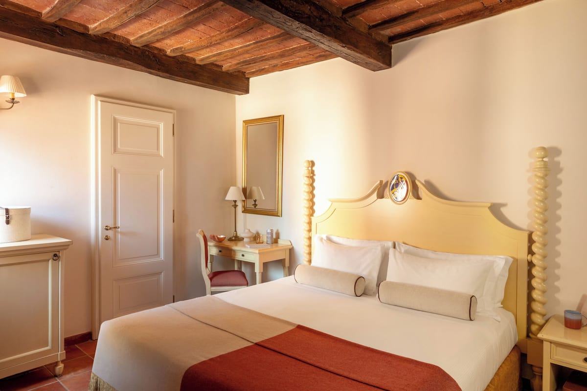 Una habitación de hotel con cama, escritorio, silla, espejo y mesita de noche.