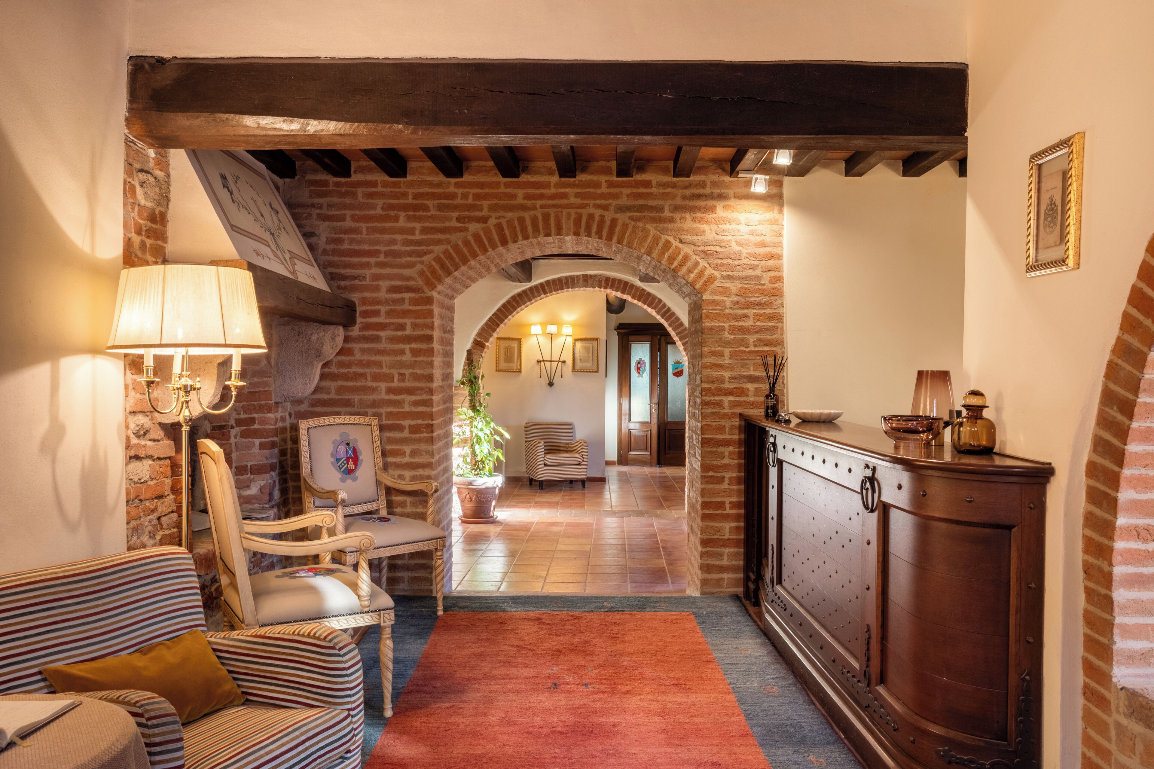 A cozy living area with a fireplace, a striped sofa, a wooden cabinet, and a brick archway leading to another room.
