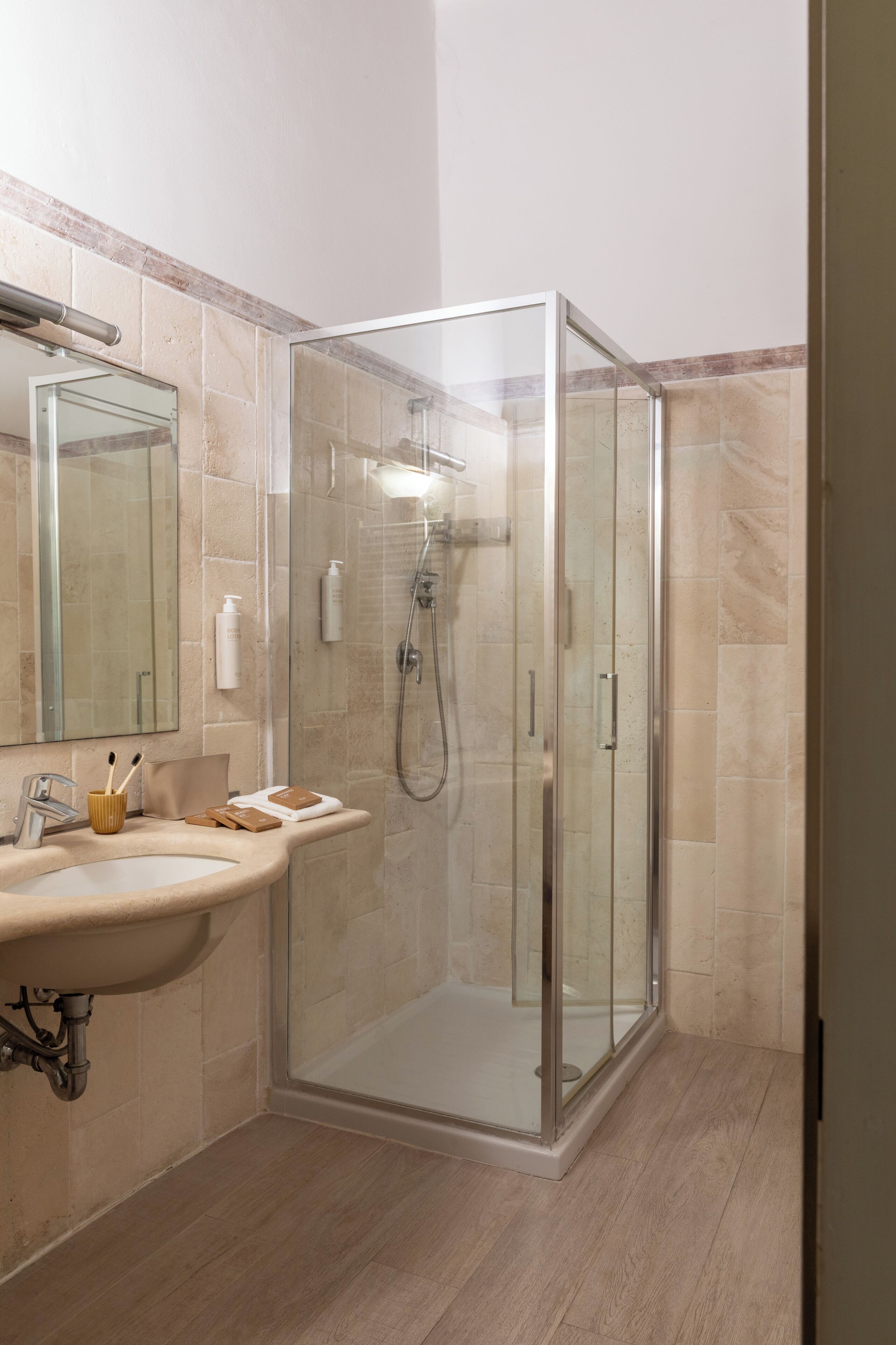 A modern bathroom with a glass-enclosed shower, a sink with toiletries, and a mirror.