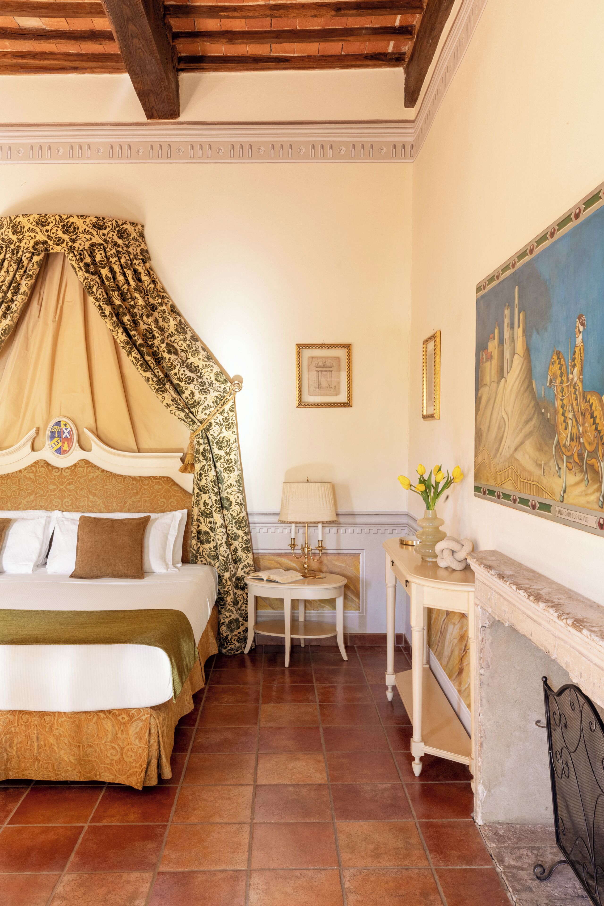 Una camera da letto con un letto a baldacchino, un tavolino con una lampada, un camino e un quadro appeso al muro.