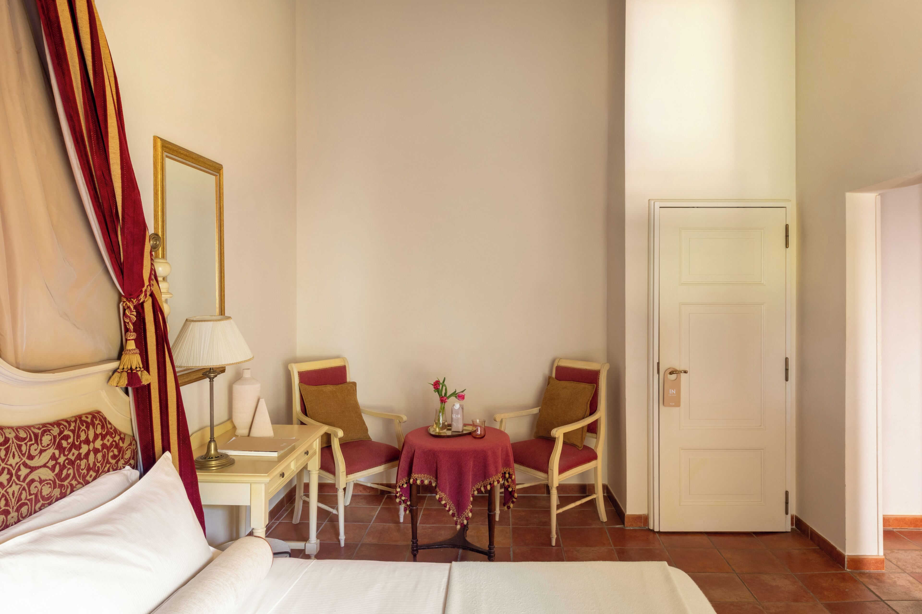 A hotel room with a bed, a table with chairs, a mirror, and a door.