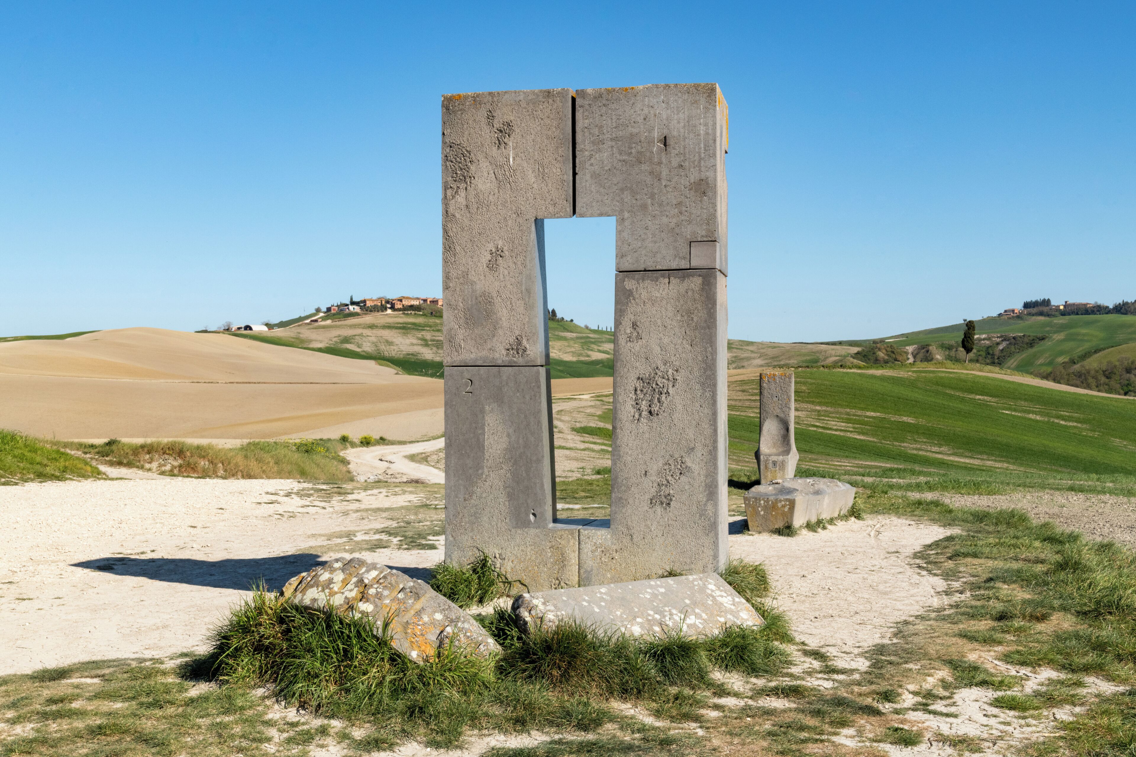 Una gran estructura de piedra con una abertura rectangular, rodeada de hierba y arena.