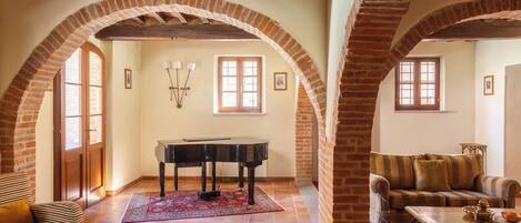 An interior with a grand piano, a sofa, and a coffee table, all under a high arched brick ceiling.