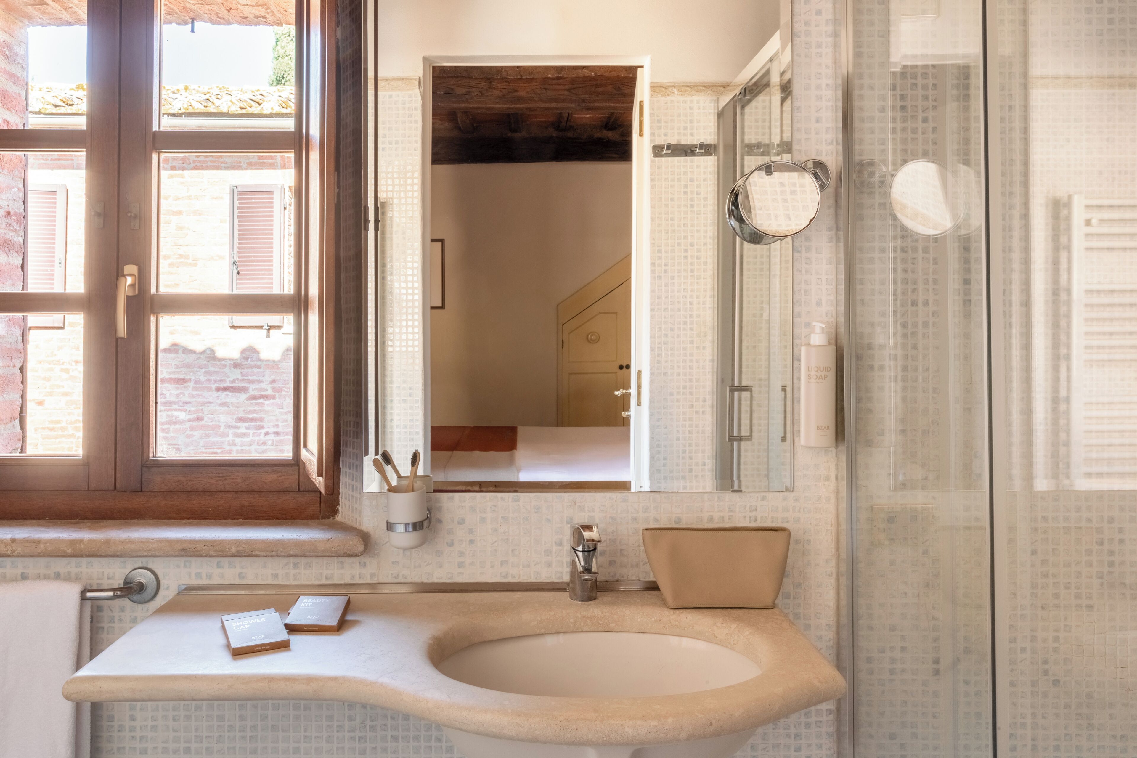 A bathroom with a large sink, a mirror, a shower, and a window.