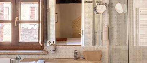 A bathroom with a large sink, a mirror, a shower, and a window.