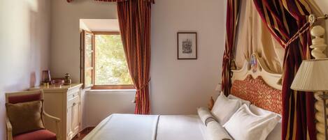 A bedroom with a bed, a chair, a bedside table, a lamp, and a window with curtains.