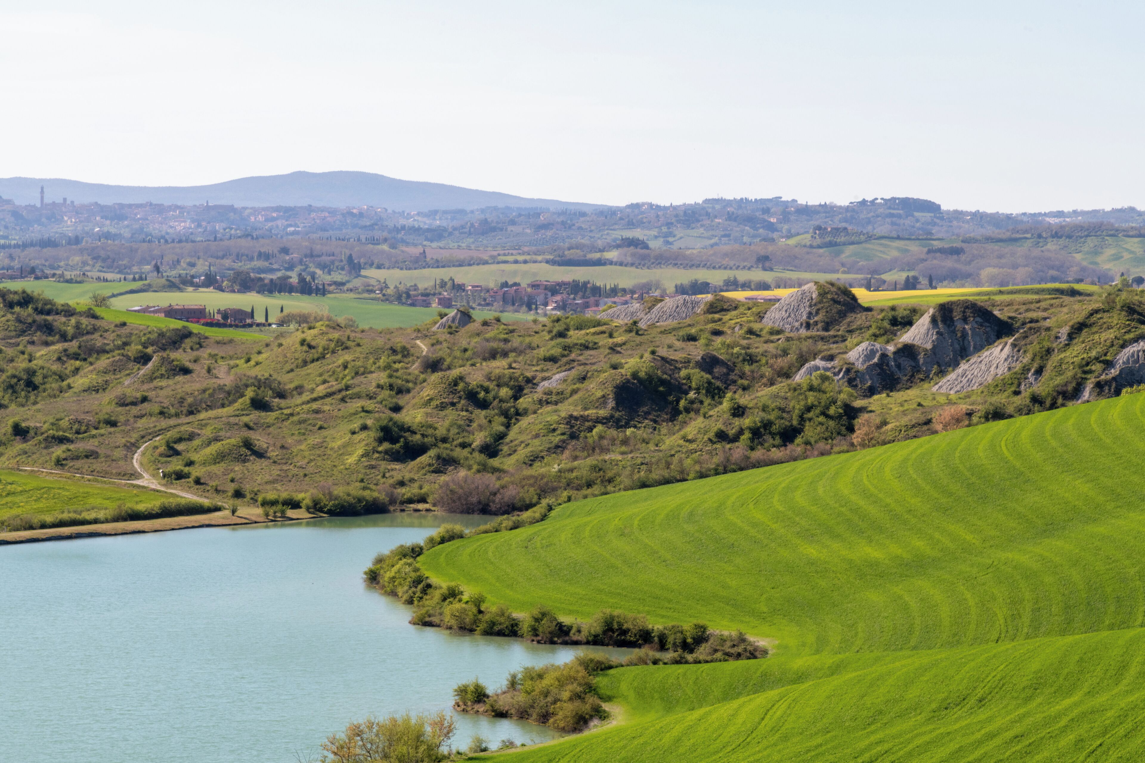 A panoramic view of a green landscape with a lake, rolling hills, and distant buildings.