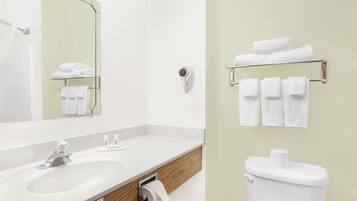 A bathroom with a white sink, mirror, and toilet. There are towels on a rack and a towel dispenser.