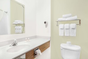 Features a large mirror, sink, and toilet with a wooden vanity and towel rack.