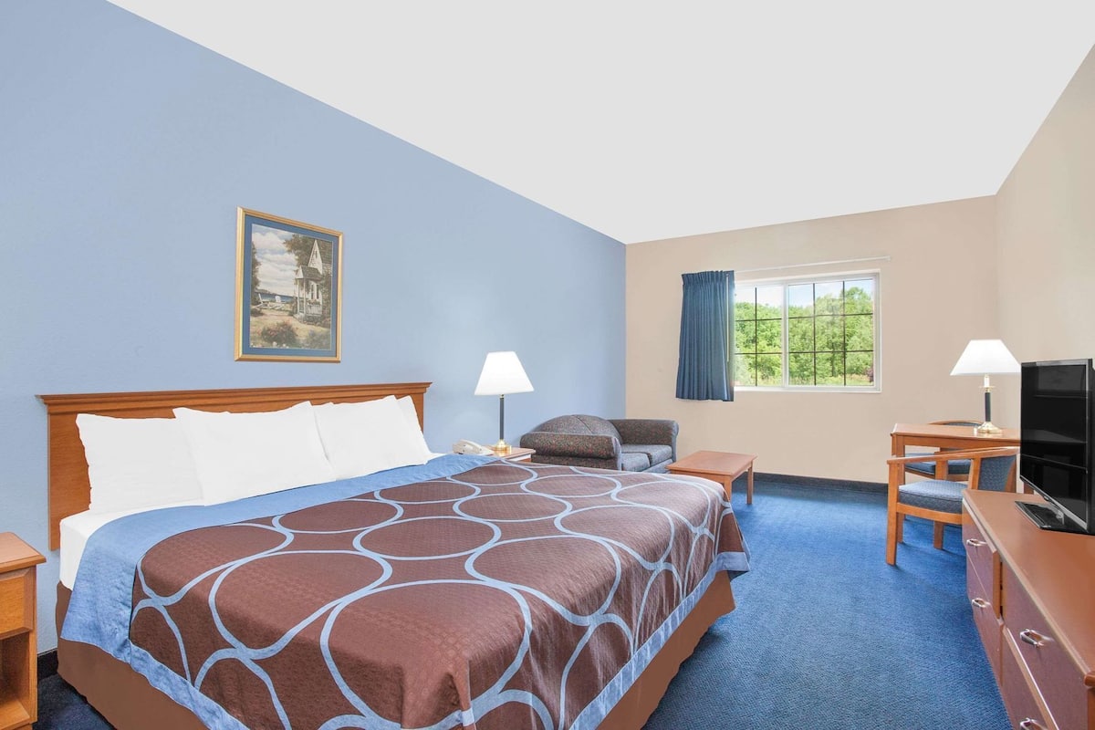 A hotel room with a large bed, a desk, a chair, a television, and a window with curtains.