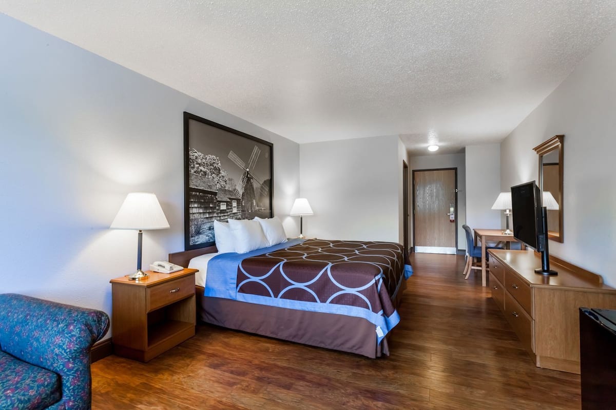 A hotel room with a bed, bedside tables, a desk, a chair, a television, and a large painting on the wall.