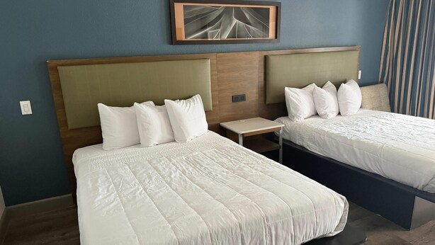 Habitación de hotel con dos camas, una mesita de noche, un enchufe y un cuadro en la pared.