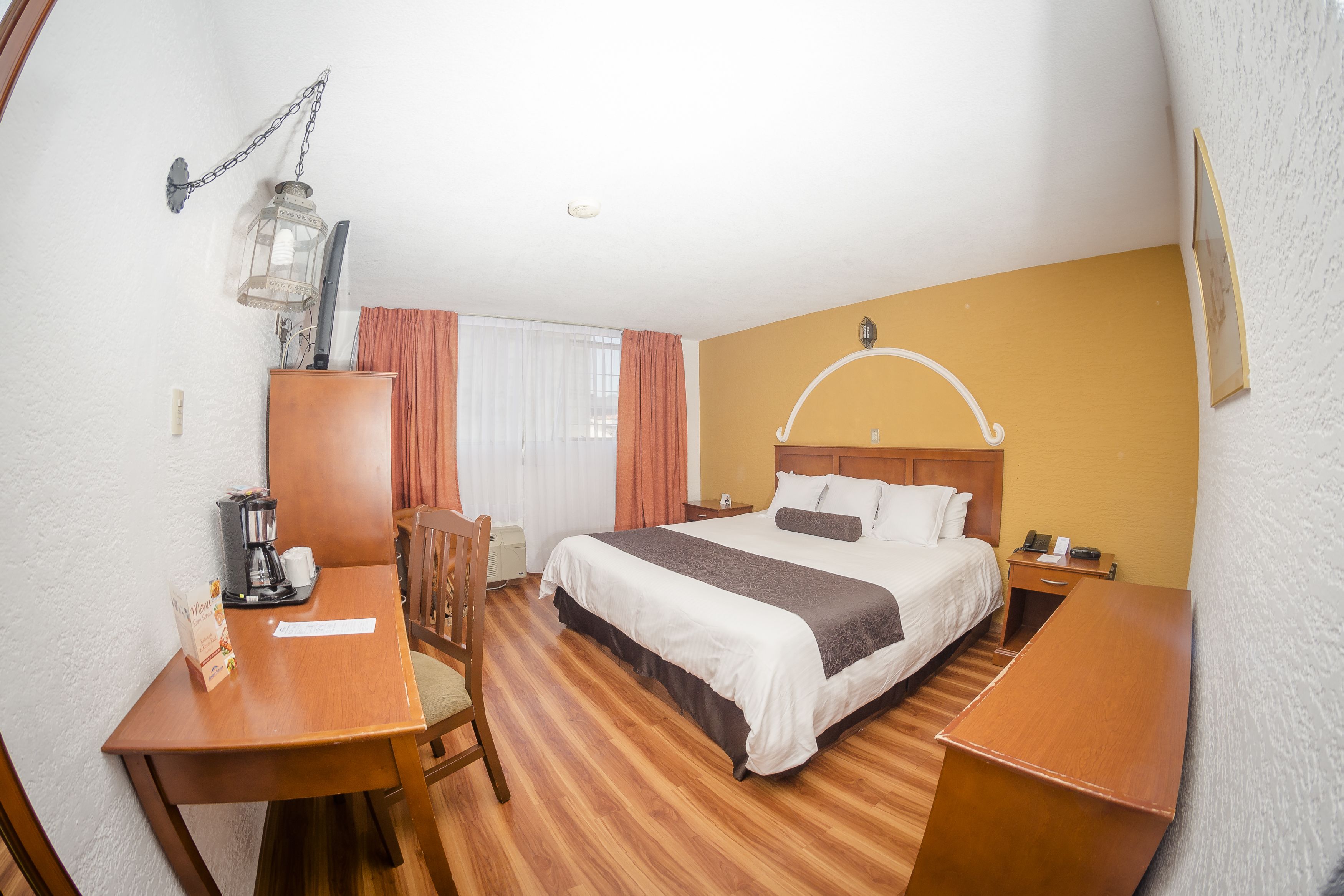 A hotel room with a bed, a desk, a chair, a coffee maker, and a nightstand.