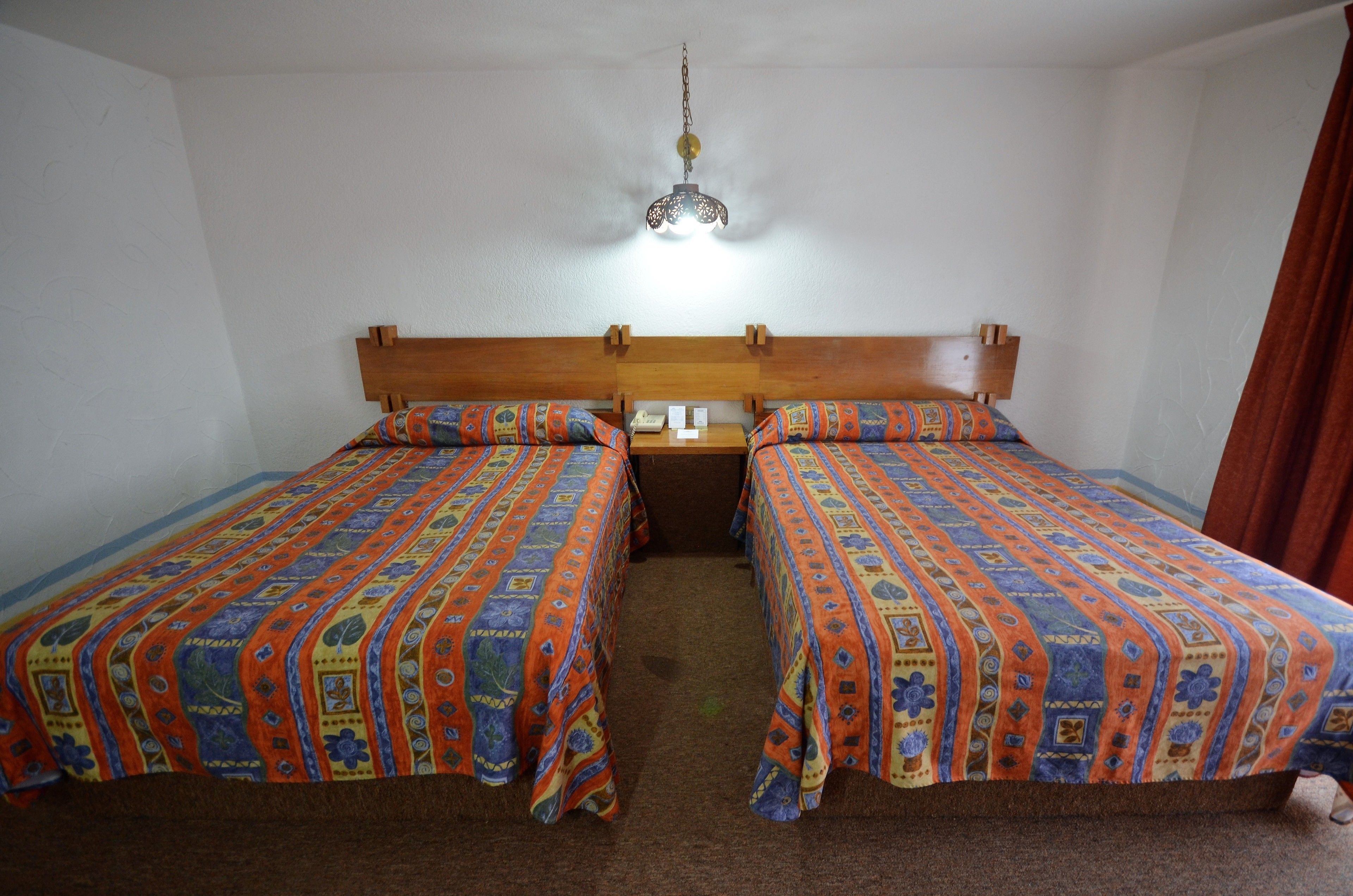 Una habitación con dos camas individuales, cada una con una colcha estampada, cabecero de madera y lámpara colgante.