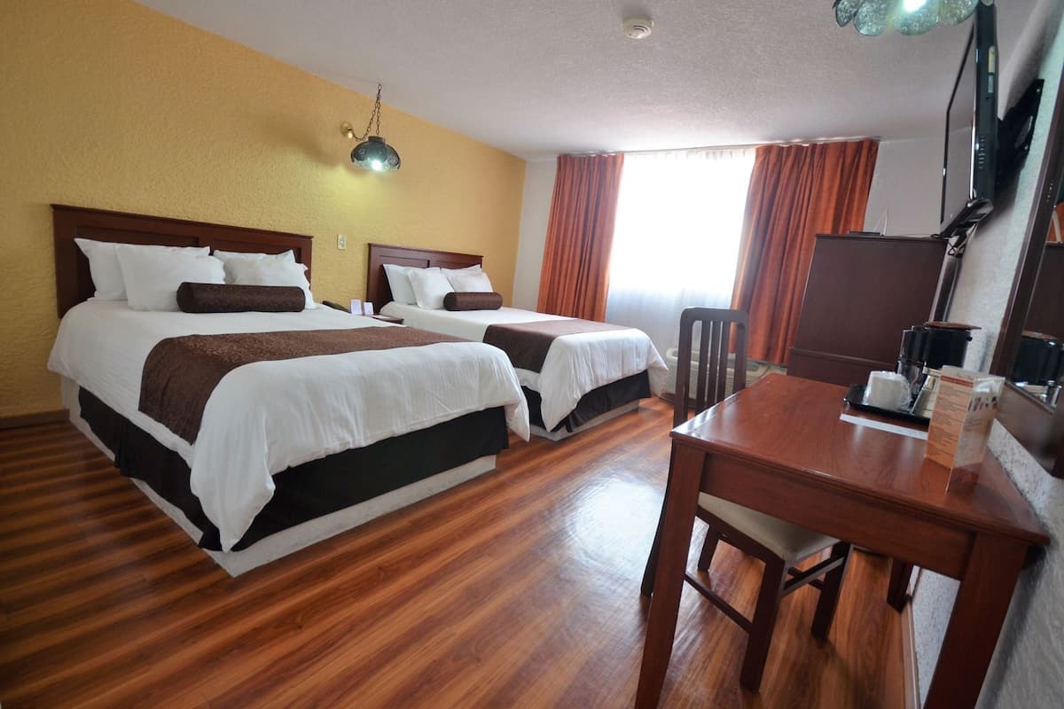 A hotel room with two beds, a wooden floor, a desk with a chair, a television, and a window with curtains.