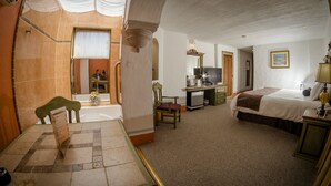 Una habitación de hotel con baño, un escritorio con televisor, una cama y una silla.