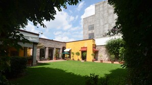 Un patio con césped verde, plantas en macetas y un edificio de fachada amarilla y detalles de piedra.
