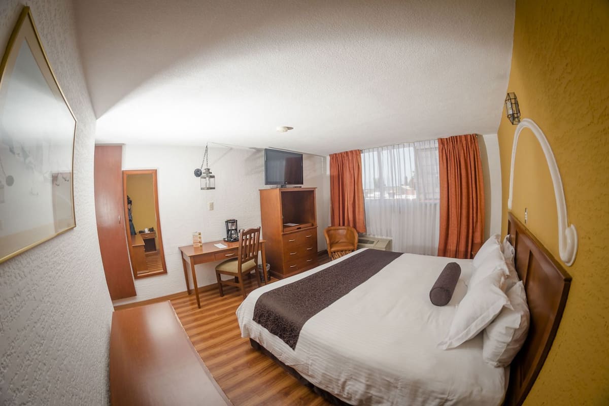 A hotel room with a bed, desk, chair, and a TV.