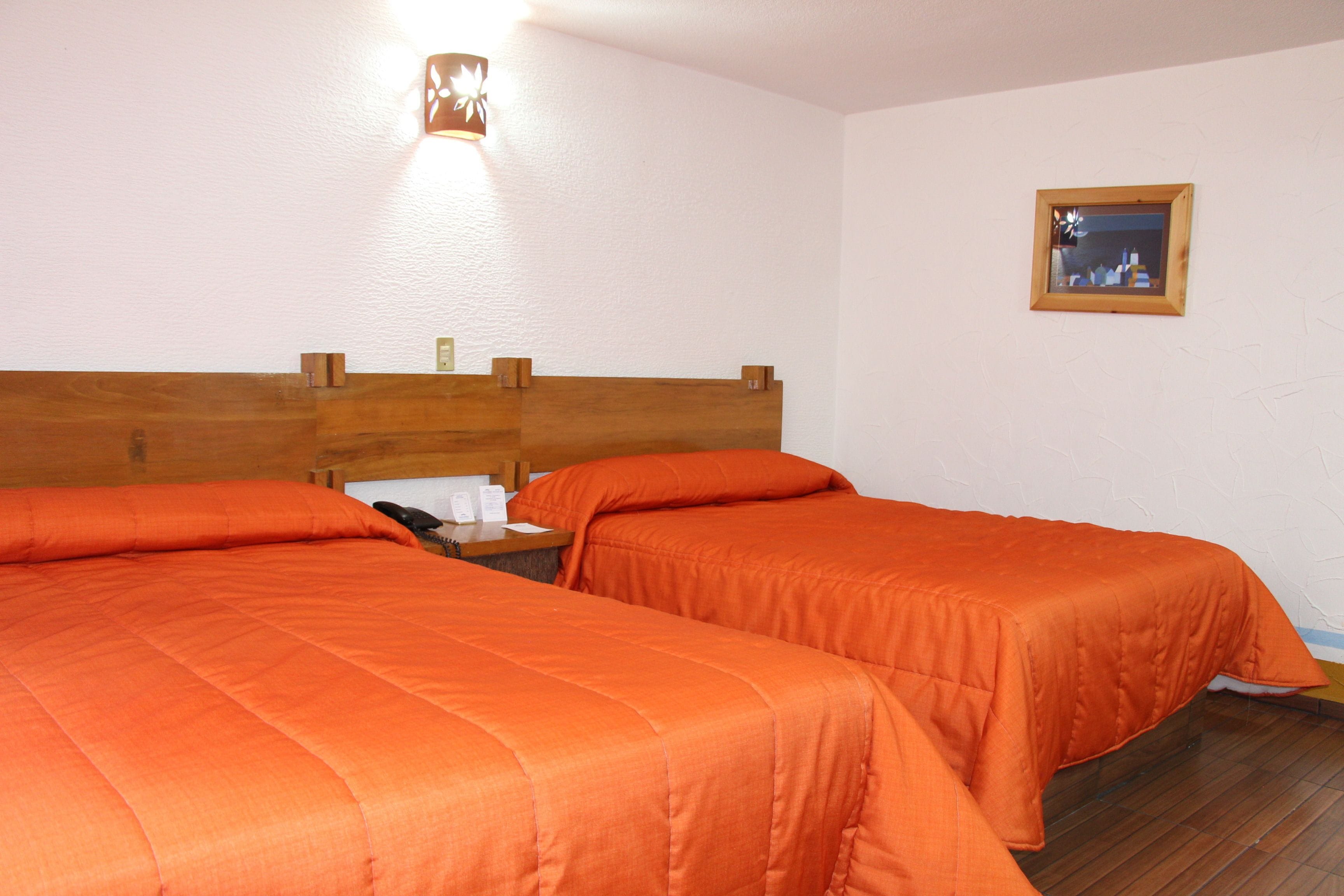 Habitación de hotel con dos camas, cabeceros de madera, una mesita de noche, una lámpara y un cuadro en la pared.