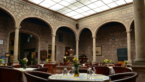 Un comedor interior con arcos de piedra, mesas dispuestas con manteles blancos y jarrones con flores.