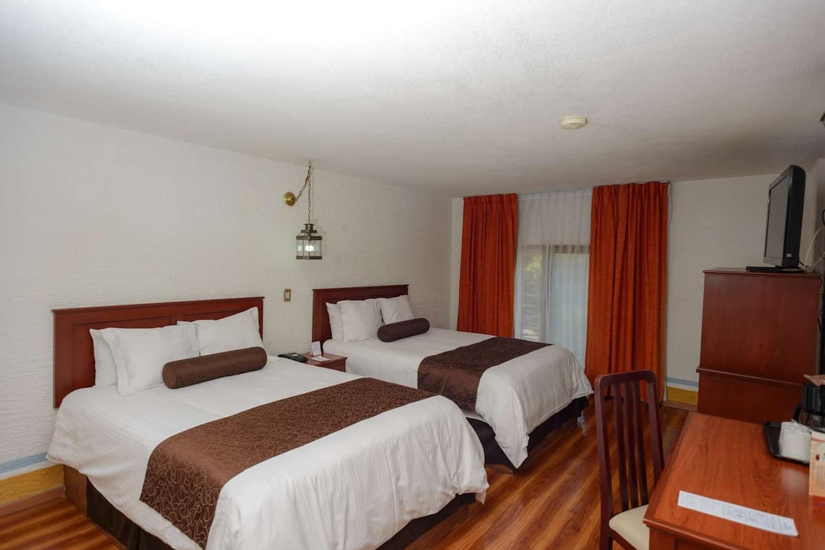 A hotel room with two beds, a wooden floor, a desk with a chair, and a television.