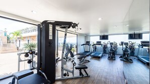 Une salle de sport moderne équipée de machines de cardio, de postes d’entraînement avec poids et d’une grande fenêtre donnant sur l’extérieur.