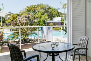 A balcony with a round table and two chairs, overlooking a swimming pool and lush greenery. - Noosa Blue Resort (Noosa Heads)