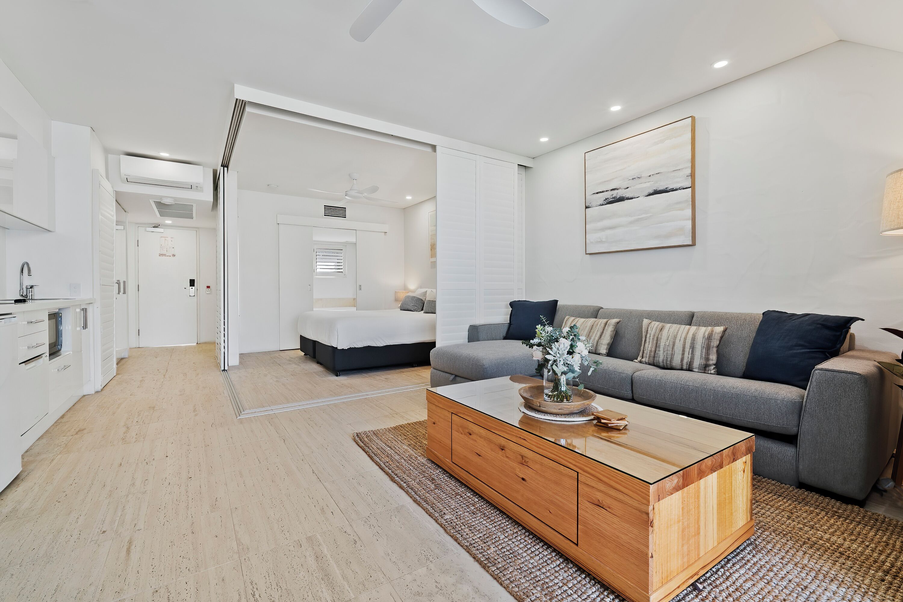 A modern living room with a grey sofa, wooden coffee table, and a painting on the wall.
