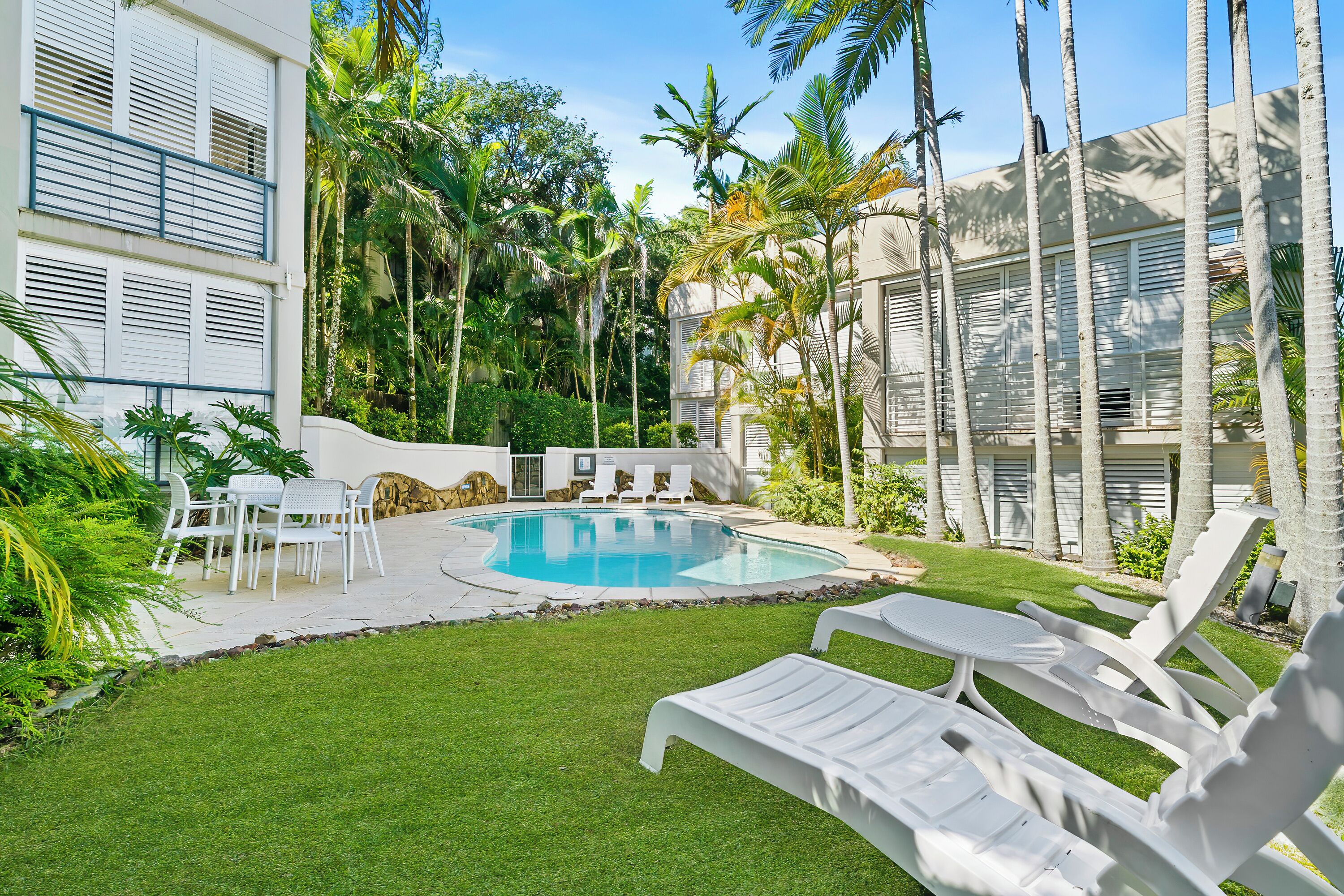 A pool area with lounge chairs, a dining set, and a well-maintained lawn.