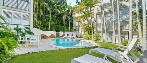 A pool area with lounge chairs, a dining set, and a well-maintained lawn.