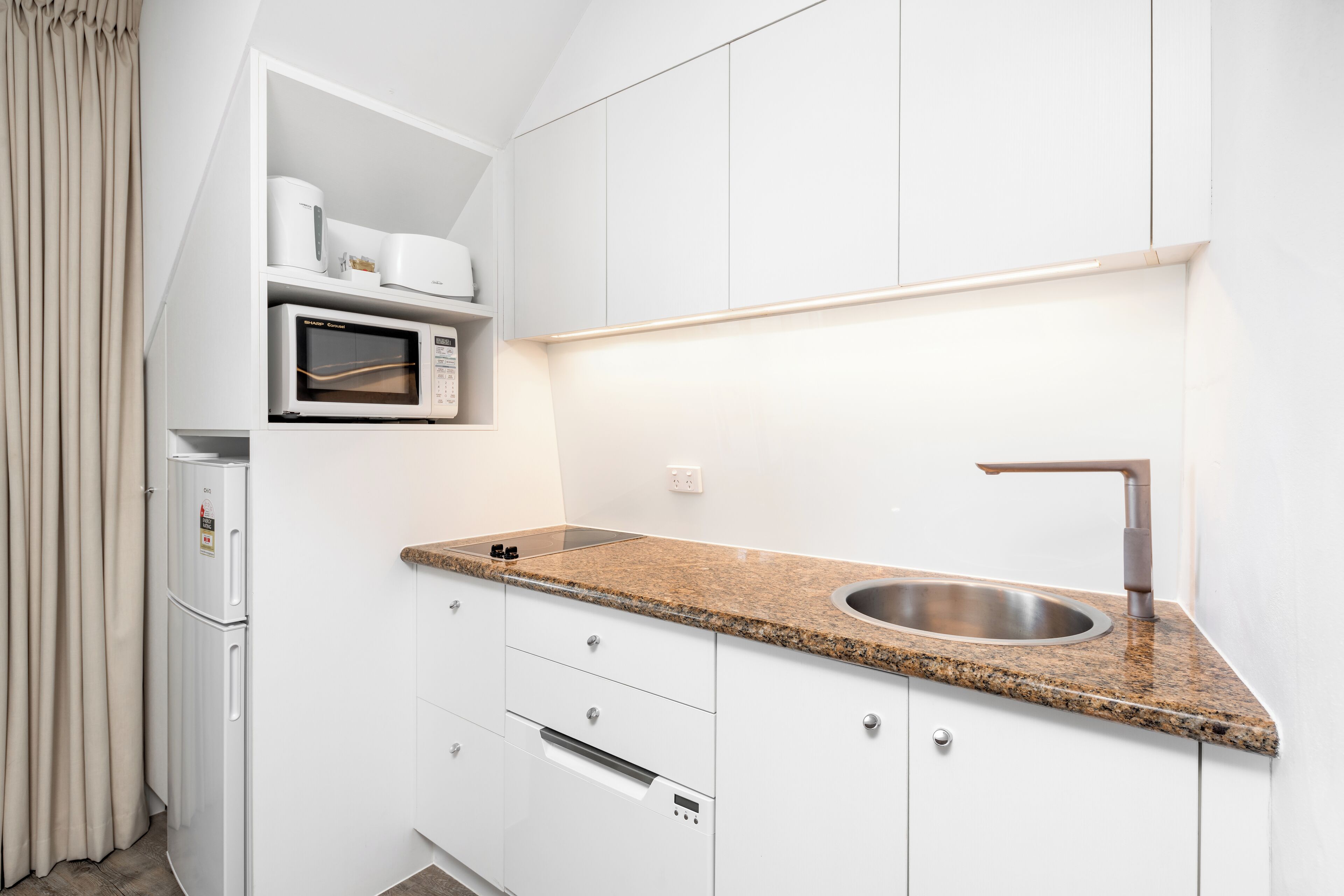 A compact kitchen with a granite countertop, stainless steel sink, and built-in appliances including a microwave and refrigerator.