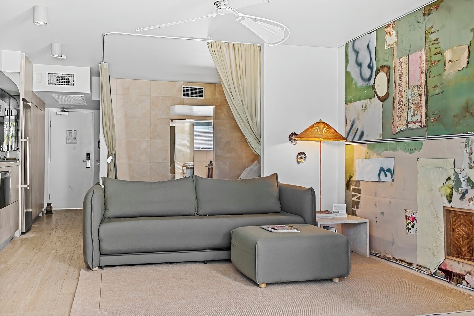 Una sala de estar moderna con un sofá gris, un pequeño reposapiés, una lámpara de pie y un cuadro en la pared.