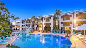 A modern hotel with a swimming pool, lounge chairs, and palm trees.