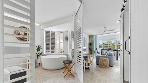 A modern, open-plan living space with a large bathtub, a dining area, and a seating area with a view of the outdoors.
