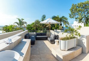 A rooftop terrace with a sofa set, a large umbrella, and potted plants. - Noosa Blue Resort (Noosa Heads)