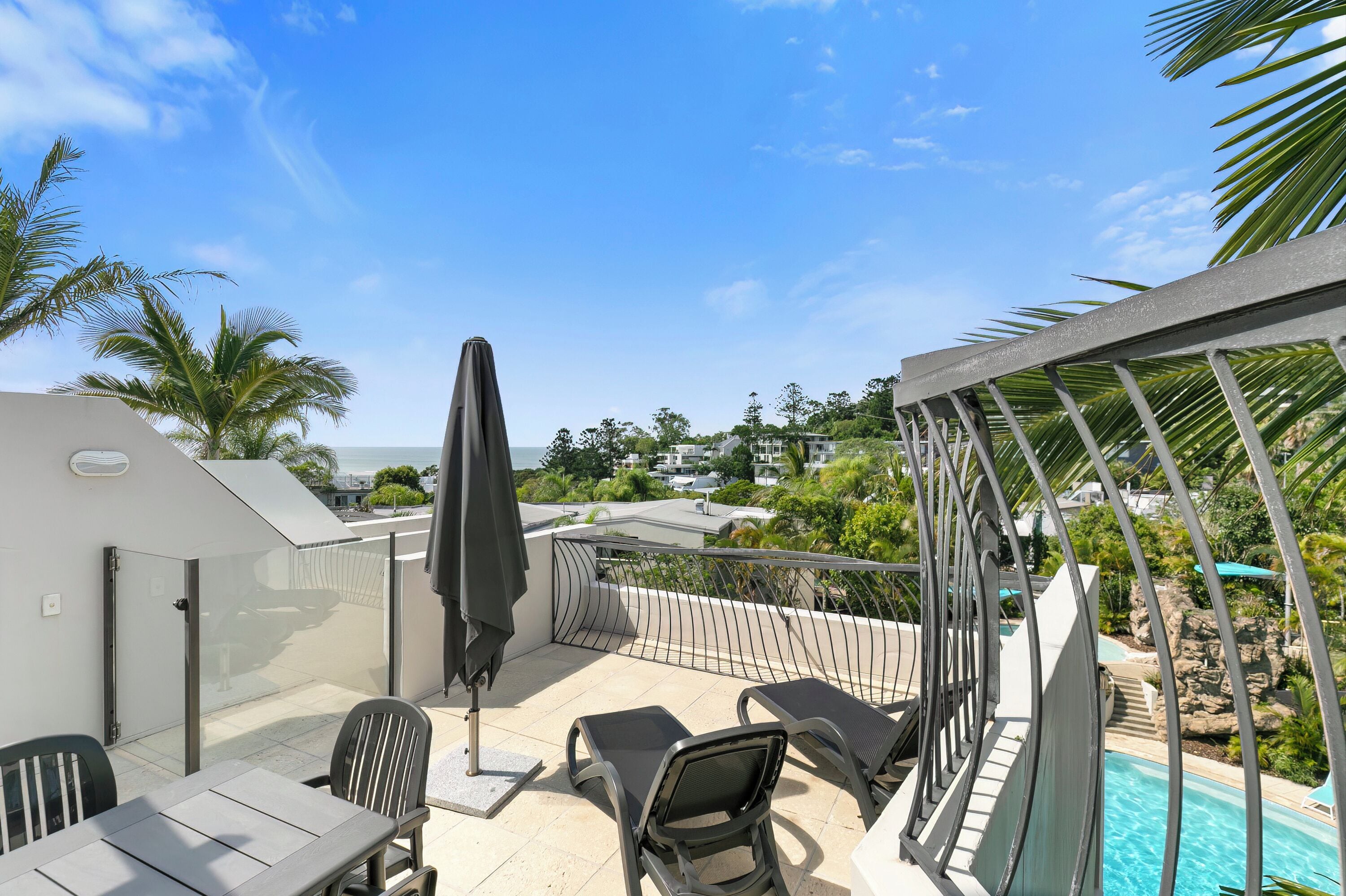 A balcony with a pool, outdoor seating, and a view of the surrounding area.