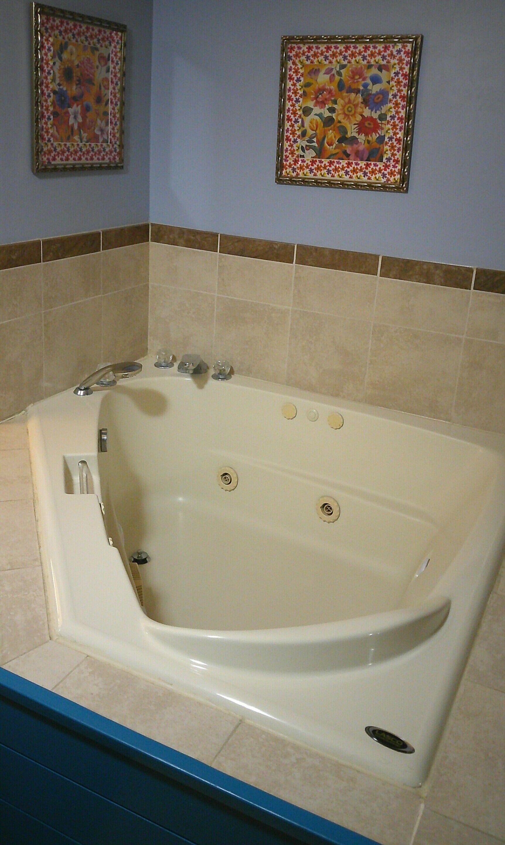A bathroom with a large bathtub, two framed floral paintings on the wall, and a tiled floor.