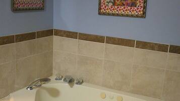 A bathroom with a large bathtub, two framed floral paintings on the wall, and a tiled floor.