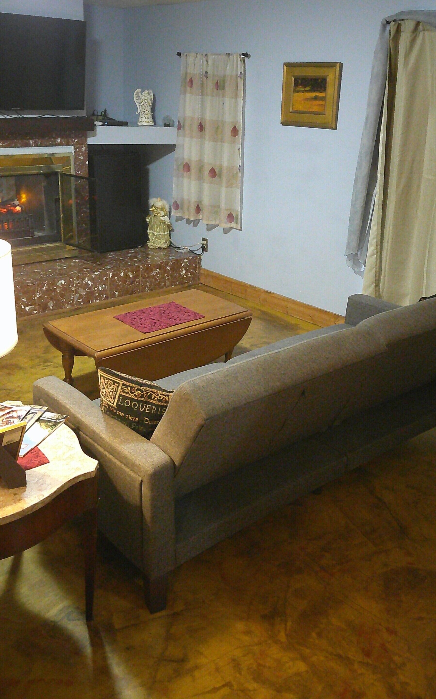 A living room with a sofa, a small table, a fireplace, and a wall with a picture and curtains.