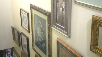 Eine Wand mit mehreren gerahmten Kunstwerken, darunter Blumen- und abstrakte Motive.