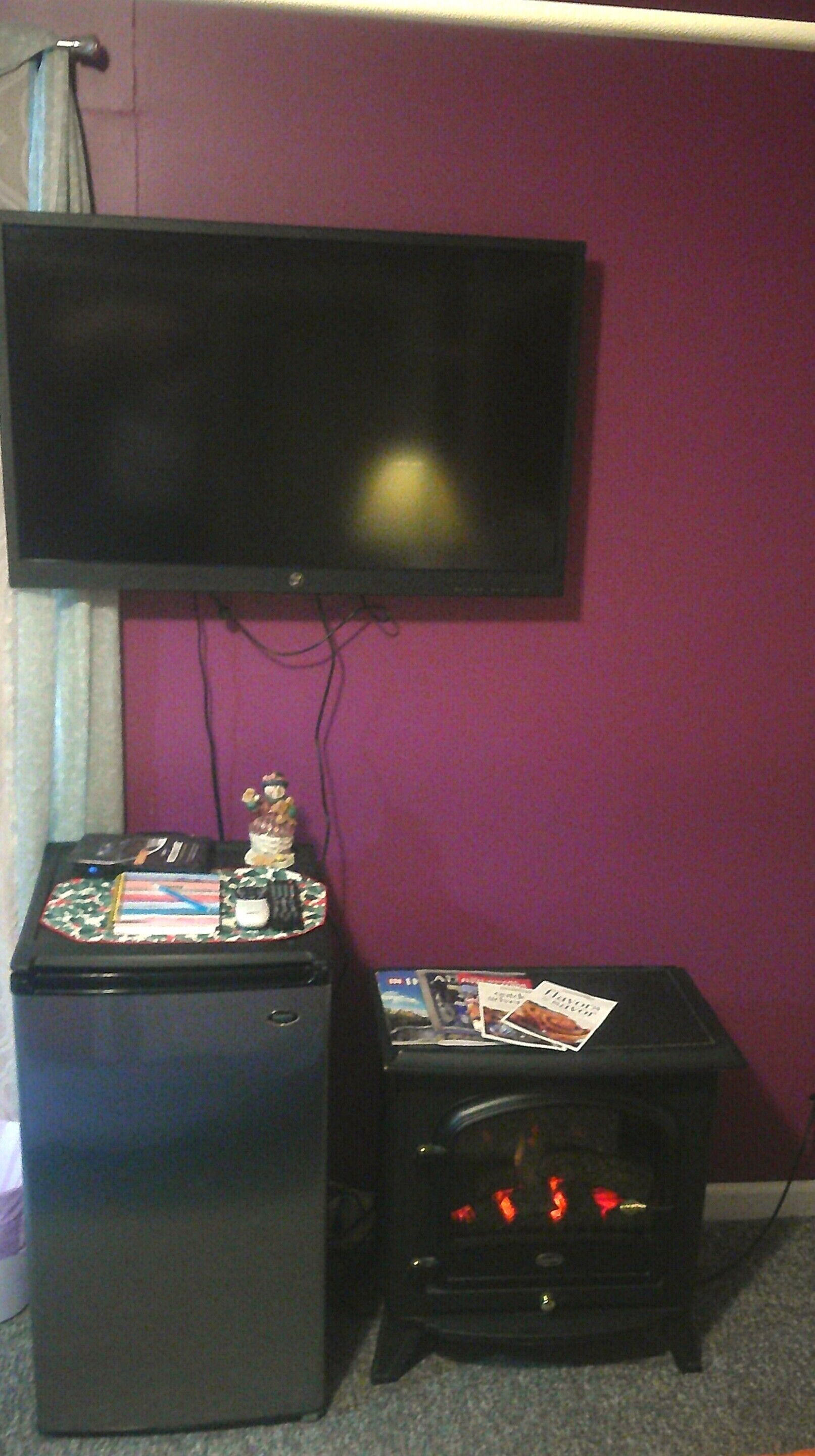 A room with a flat-screen TV mounted on the wall, a small refrigerator, and a coffee machine.