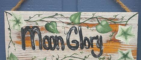 Uma placa de madeira com o texto 'Moon Glory' e trepadeiras decorativas.