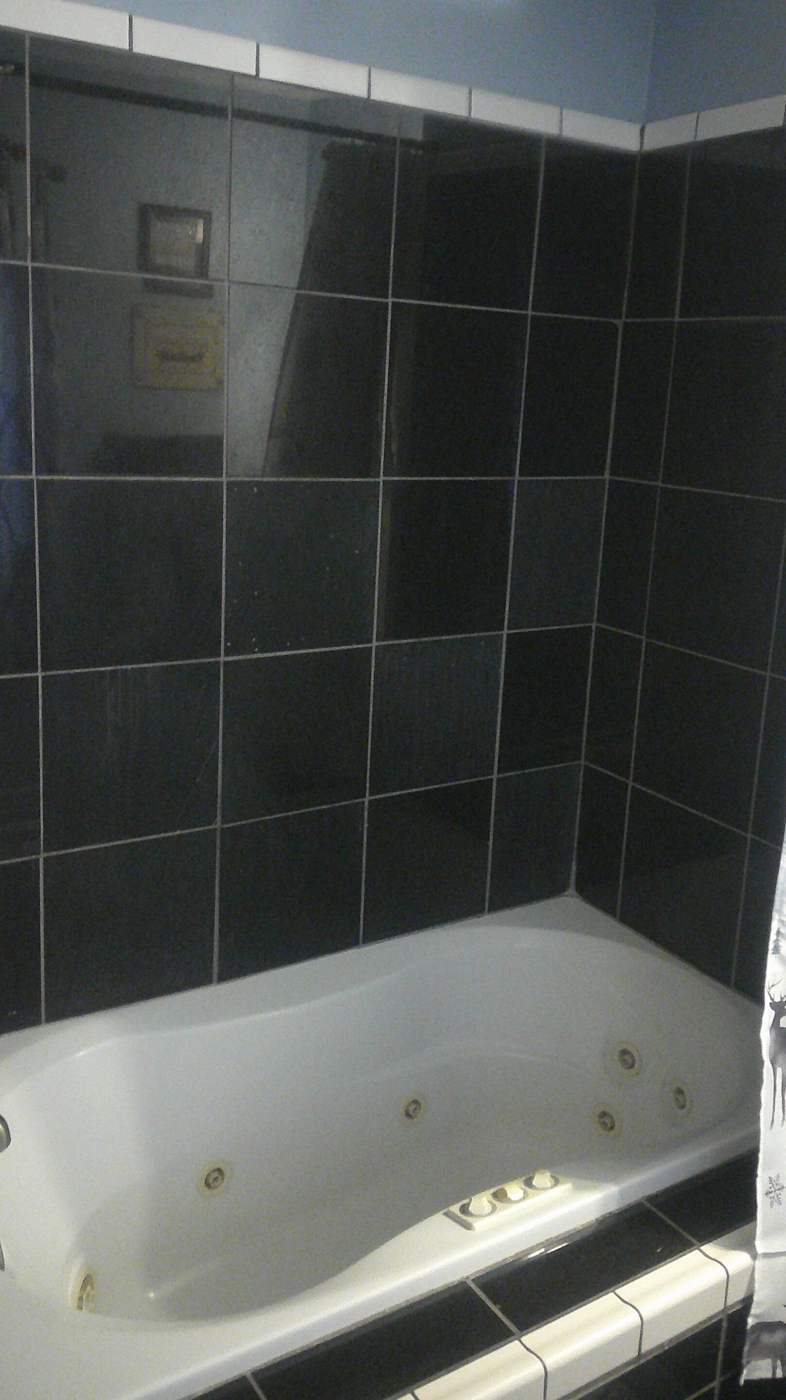 A bathtub with a white interior, surrounded by black tiles.
