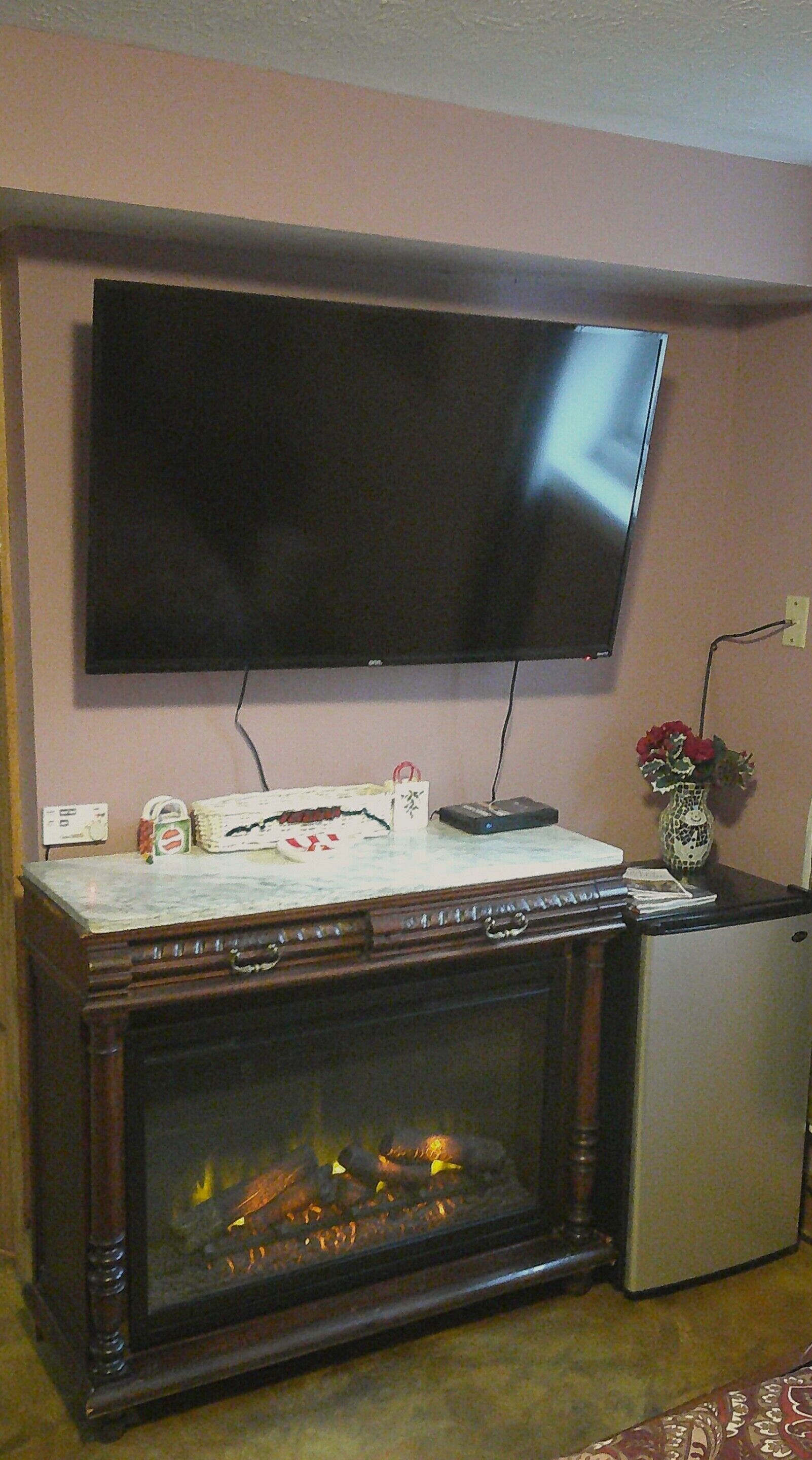 Een woonkamer met een flatscreen televisie aan de muur, een open haard en een kleine koelkast.