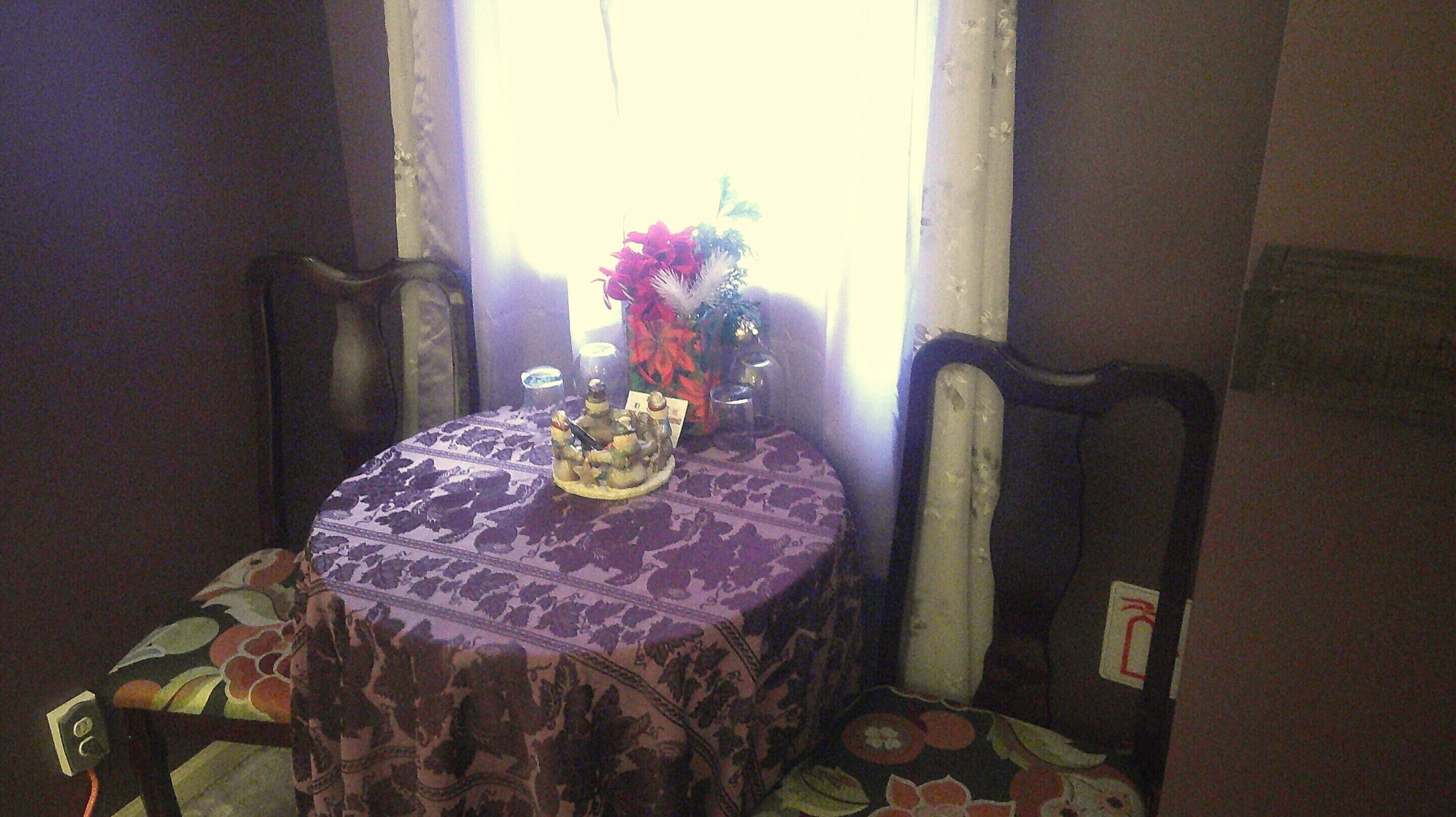 A dining table with a floral tablecloth, chairs with cushioned seats, and a vase with flowers.