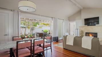 A modern living room with a fireplace, a TV mounted above it, and a dining area with a table and chairs.