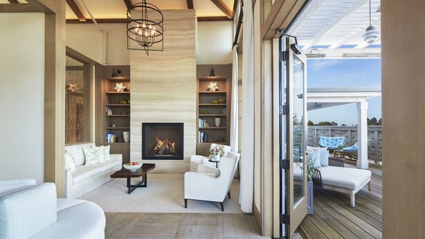 A spacious living room with a fireplace, white sofas, and a wooden deck.