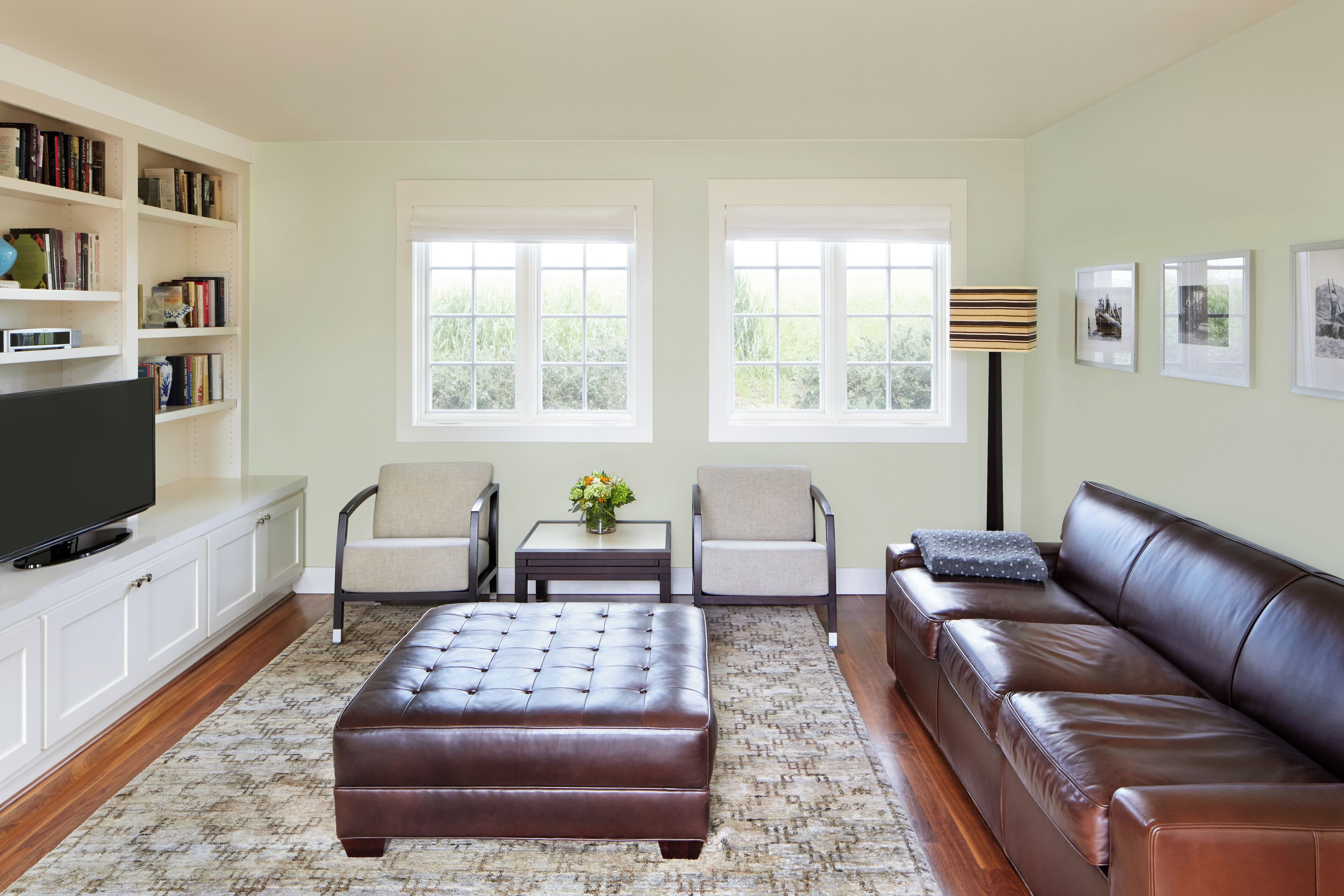 A living room with a brown leather couch, two armchairs, a coffee table, a television on a cabinet, and a bookshelf.