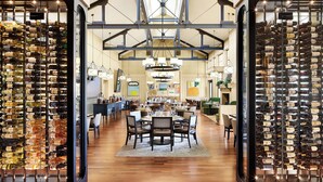 A spacious dining area with high ceilings and exposed beams, surrounded by wine racks filled with bottles.